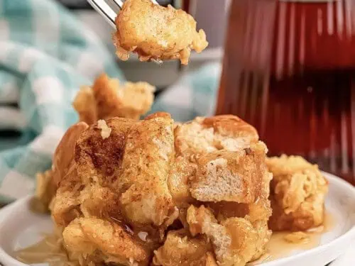 fork full of french toast casserole above a plate of casserole.